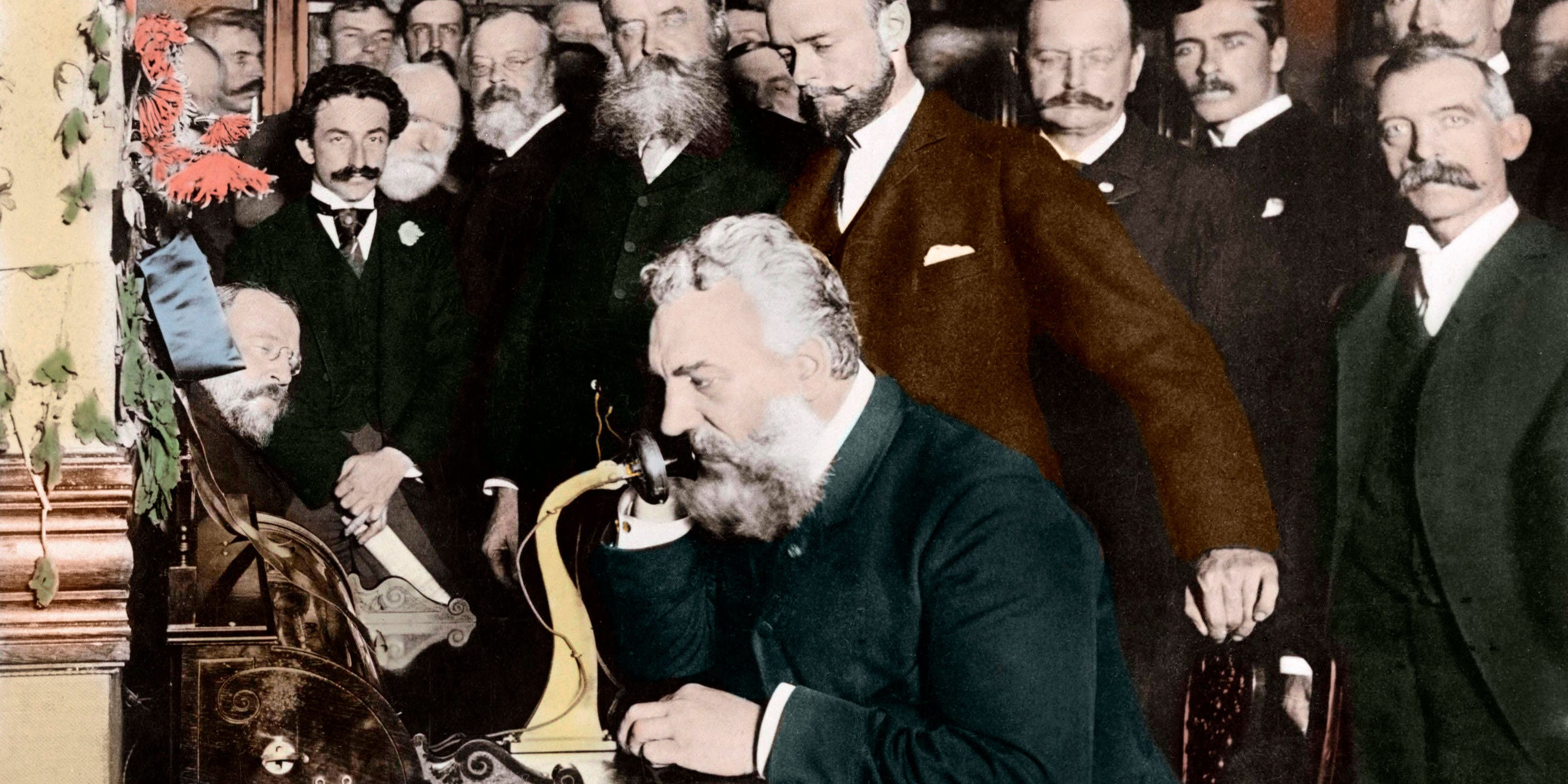 A group of businessmen watch inventor Alexander Graham Bell as he opens the New York-Chicago telephone line.