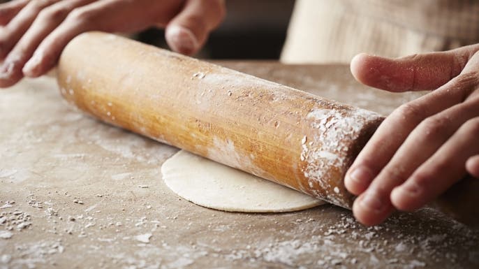 Hands baking dough with rolling pin on wooden table