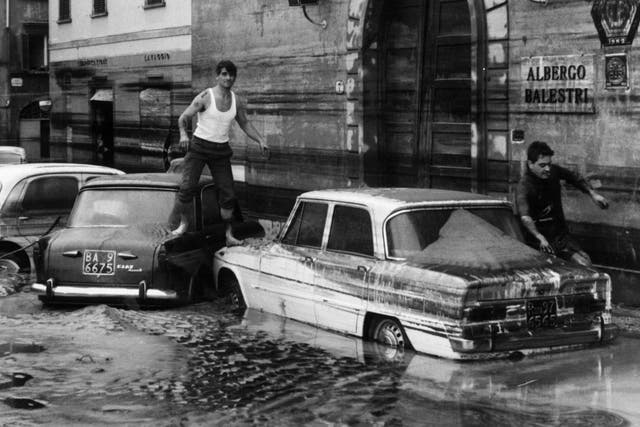 7th November 1966: Pedestrians use marooned cars as stepping stones in the flooded streets of Florence after the River Arno had burst its banks.