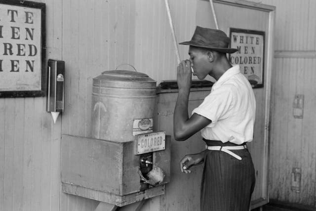 A man drinking water at a water cooler labeled 'Colored' in a bus terminal in Oklahoma City, Oklahoma, July 1939.