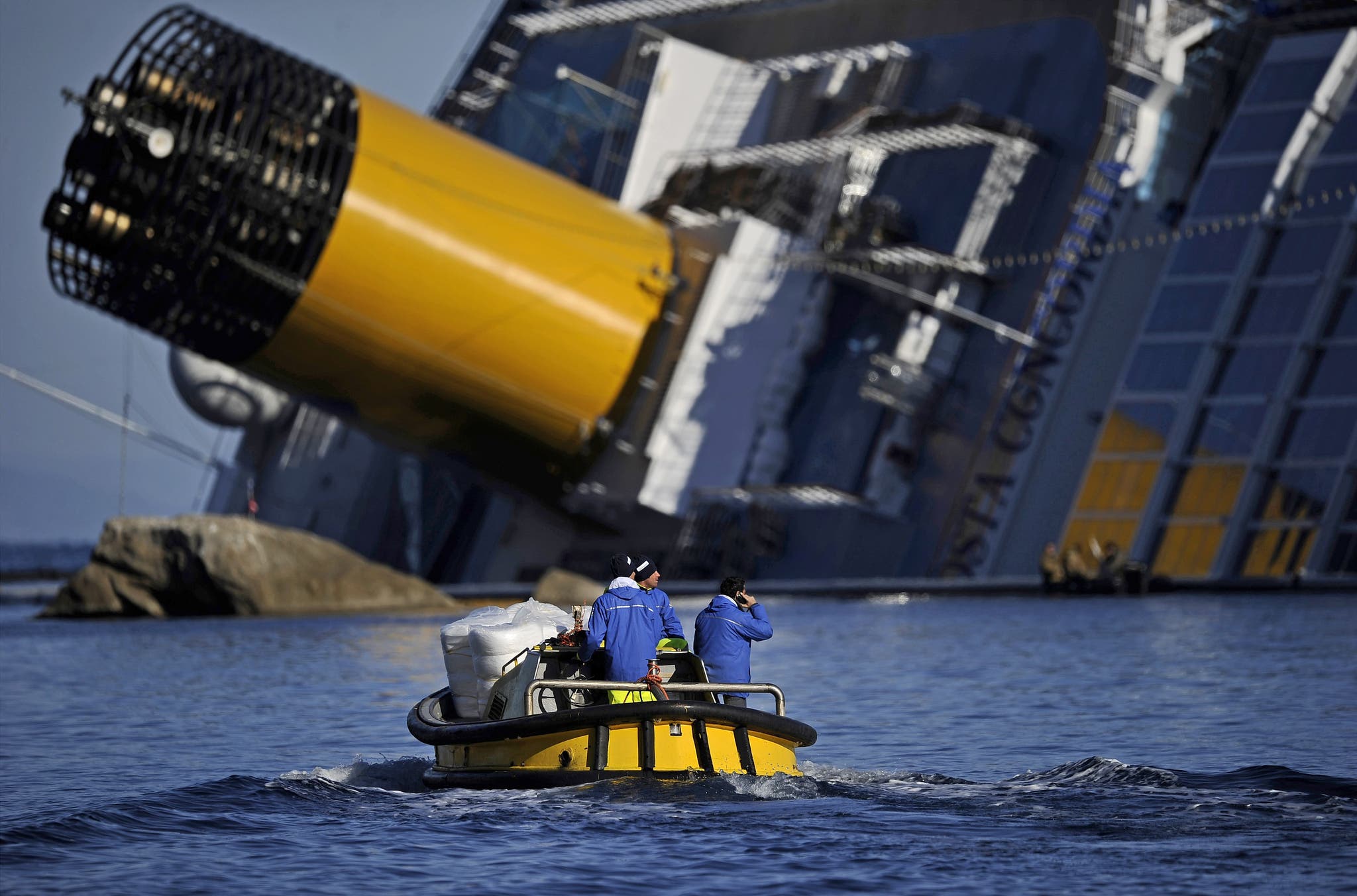 Technicians pass in a small boat near the stricken cruise liner Costa Concordia lying aground in front of the Isola del Giglio on January 26, 2012 after hitting underwater rocks on January 13.